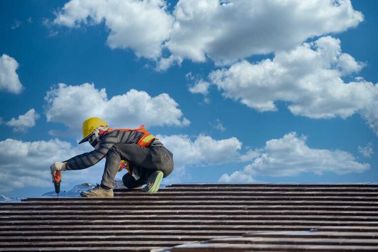 A person checking attic insulation and ventilation with a flashlight on an unfinished wooden roof structure.