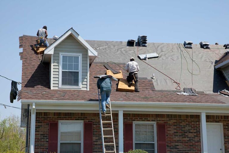 A person using a roof rake to remove leaves from a residential roof in late autumn.